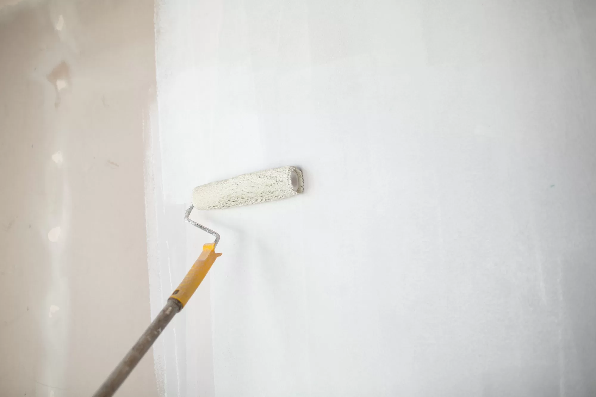 White paint roller in hand with drywall wall painting